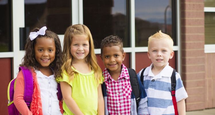 4 elementary age students smiling in front of a school building