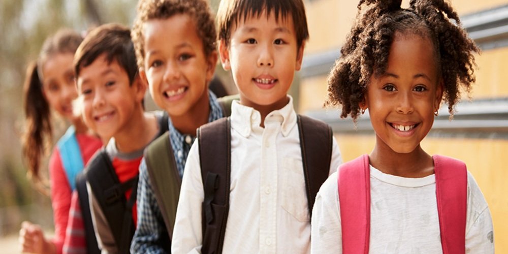 diverse group on young children lined up near a school bus