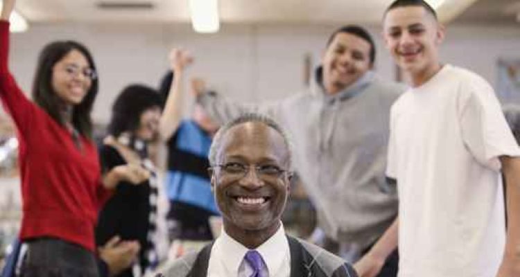 Male teacher smiling surrounded by high school students