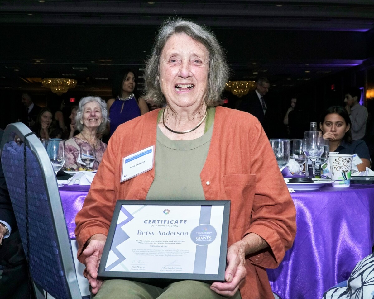 Co-founder Betsy Anderson displays her certificate, seated at a table